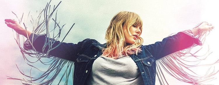 A woman with blond hair wearing a denim jacket with fringe stands outdoors, arms outstretched, looking down with a serene expression against a cloudy sky.