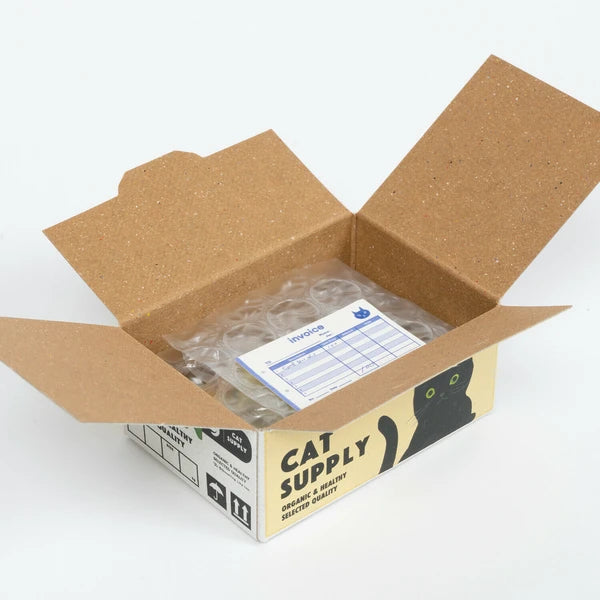An open cardboard box labeled "Japanese Mini Sticker Box Cat Supplies" by Blue Dog Posters, featuring a black cat illustration and containing bubble wrap with an invoice on top of the packaging inside.