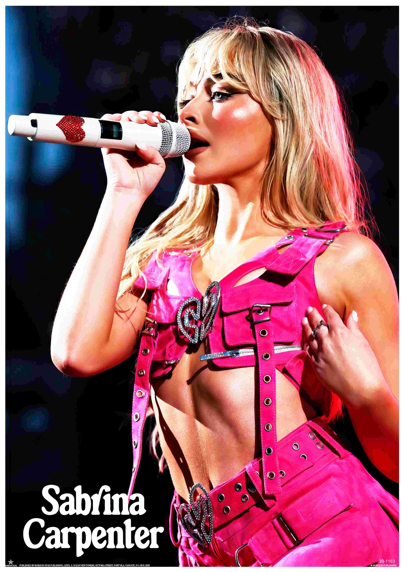 Sabrina Carpenter performs on stage in a pink outfit with heart buckles, holding a white mic with red hearts. This vibrant A3 poster, "Sabrina Carpenter Pink" by Blue Dog Posters, is printed on premium 250gsm Satin Paper. Her name appears below in bold white letters.