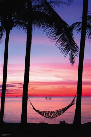 A hammock hangs between two palm trees silhouetted against a vibrant sunset. The sky displays a gradient of pink, purple, and orange hues, reflected in the calm ocean below. A boat is visible on the horizon, enhancing the serene tropical scene depicted in this Beach - Sunset from the NAT 001 Collection printed on premium 150gsm gloss paper.