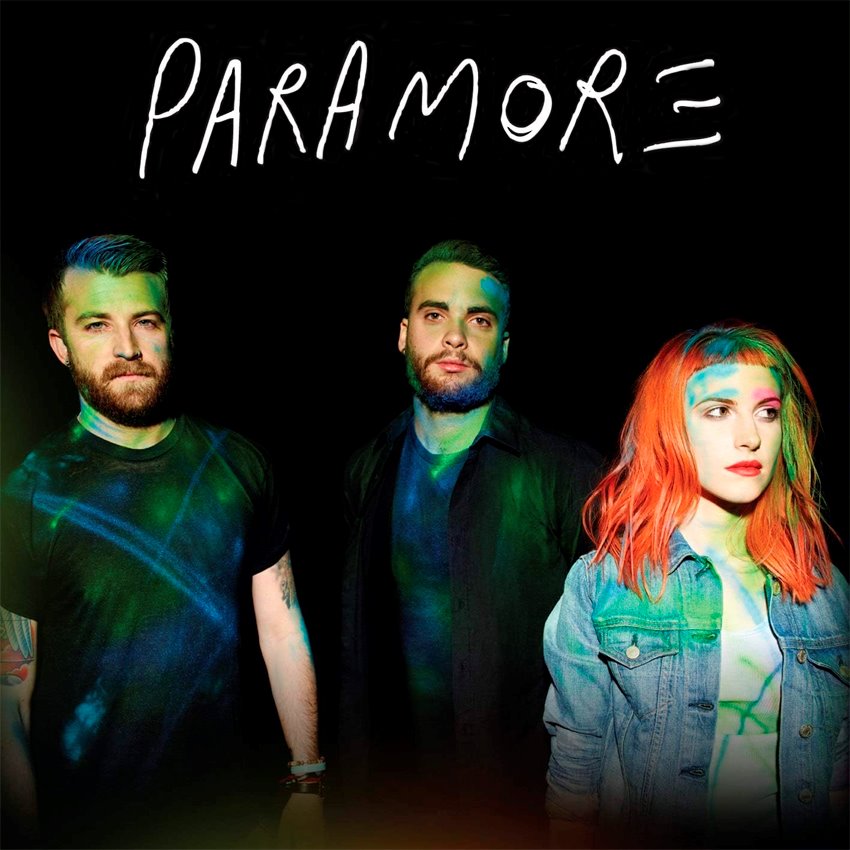 Three band members stand against a dark background with colorful light projections. "Paramore" is written above them in white. On the right, one member has vibrant red-orange hair and wears a denim jacket. (Product: Paramore - Album 30x30cm by MUS).