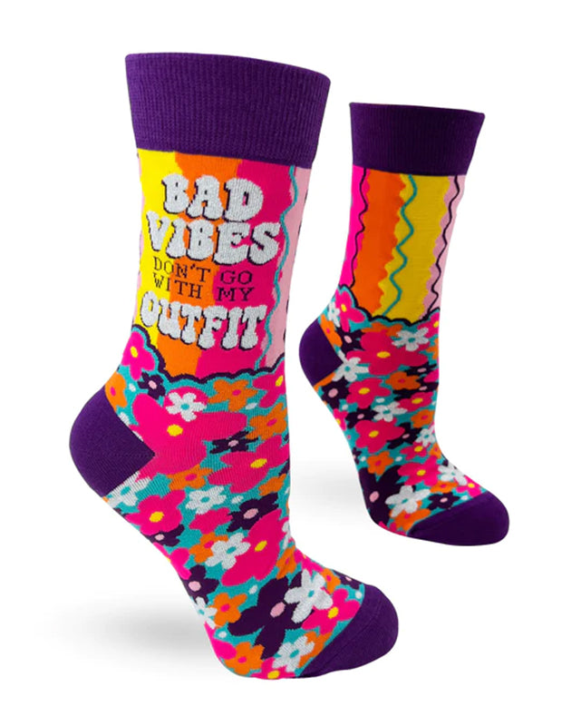 Introducing the Bad Vibes Socks Ladies by Blue Dog Posters—a pair of colorful crew socks featuring dark purple cuffs, heels, and toes. These stylish socks boast vibrant, multicolored floral patterns and wavy lines. One sock displays the bold white text: "Bad vibes don't go with my outfit." Comfortable and trendy, they fit women's shoe sizes perfectly and are machine wash friendly.