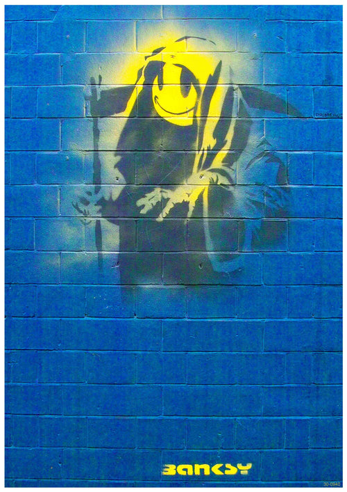A piece of street art titled "Banksy Grin Reaper" is displayed on a blue brick wall, featuring a yellow, smiling Grim Reaper holding a scythe. The signature "Banksy" is stenciled in yellow at the bottom of the artwork, reminiscent of the high-quality Satin Paper used in Y’s A3 Posters.
