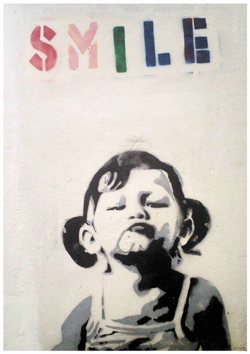 A stencil graffiti of a young child with pigtails, making a playful, exaggerated pouty face. Above the child, the word "SMILE" is spray-painted in colorful, block letters. The backdrop is a plain, light-colored wall. This captivating Banksy Smile Little Girl design by Brand Y can be stunningly captured on A3 posters printed on 250gsm satin paper.