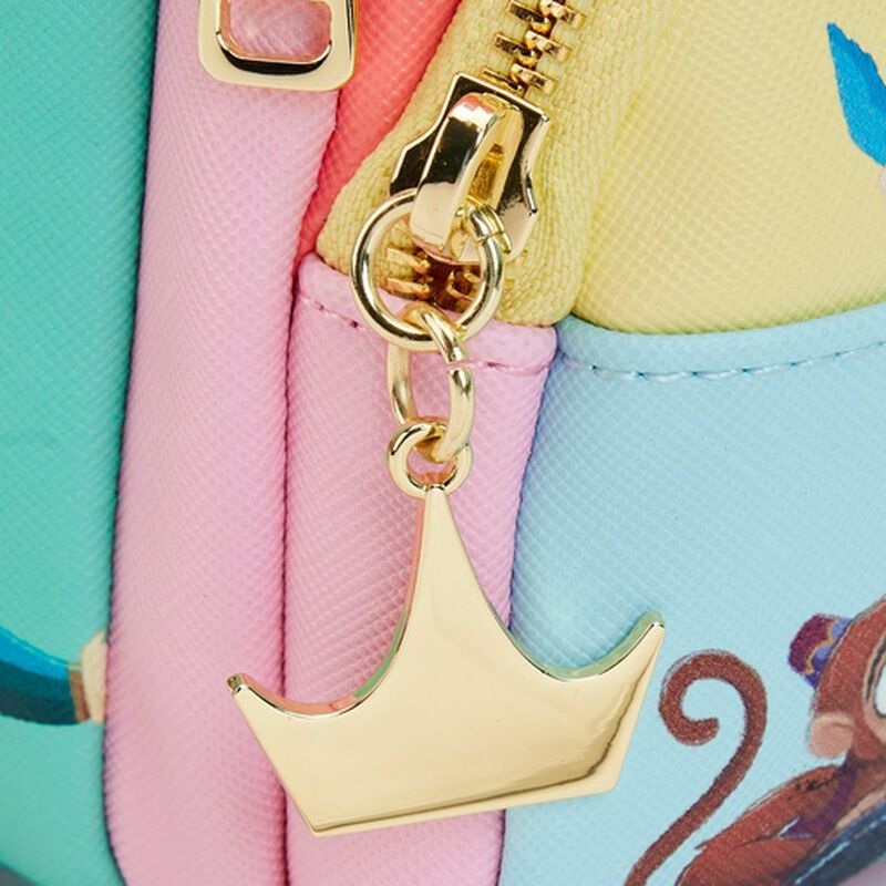 Close-up of the Disney Princess Collage Mini Backpack by Blue Dog Posters, featuring vibrant pastel sections in teal, pink, and yellow. A gold crown-shaped charm reminiscent of a Disney Princess adorns the zipper, while a playful partial design of a cartoon monkey tail accents the bag.