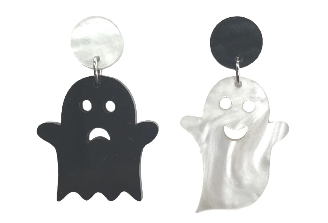 Two pairs of Ghost Earrings Happy Sad Face from Blue Dog Posters hang side by side. The left earring is black with a sad expression, while the right one is white with a happy face. Both handmade ghosts dangle from circular studs; the black ghost from a white stud and the white ghost from a black stud.