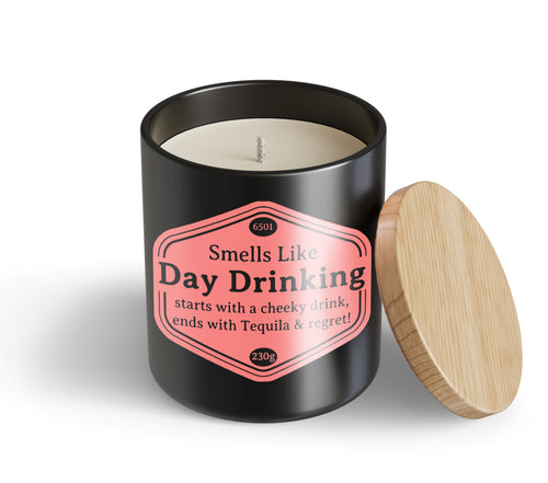 The Day Drinking Candle Hustle & Co by Blue Dog Posters features a black jar with a wooden lid. The label reads: "Smells Like Day Drinking—starts with a cheeky drink, ends with Tequila & regret!" Lid rests beside the candle.