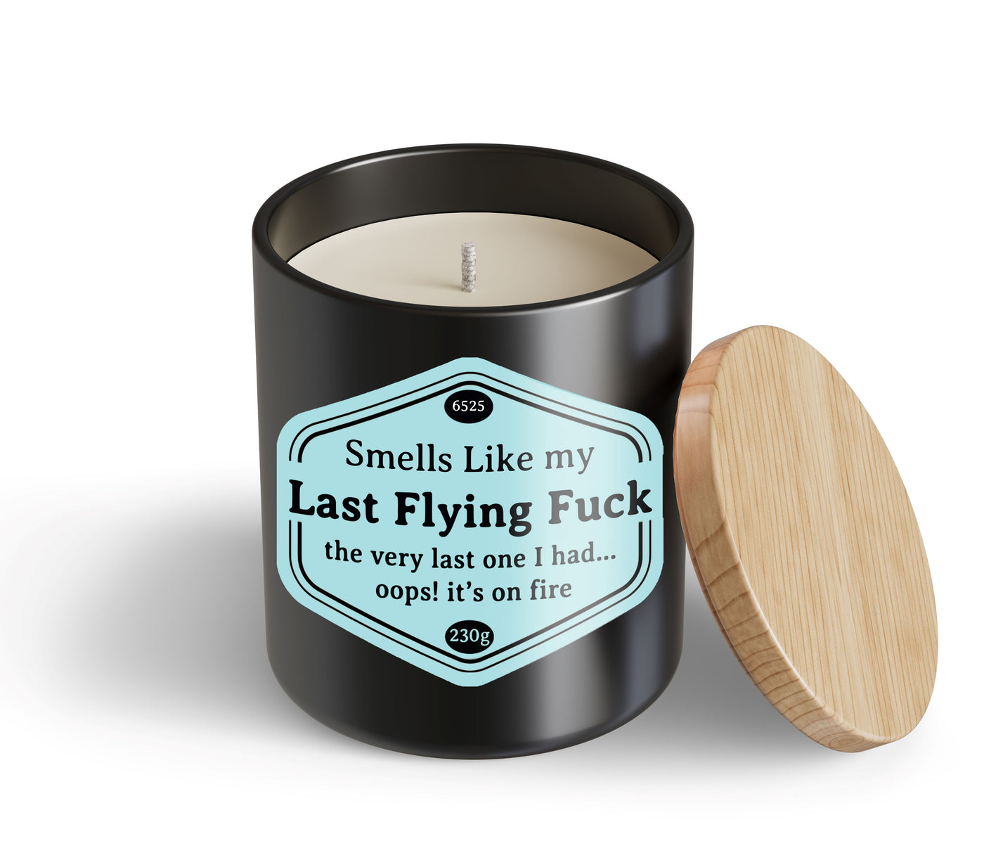 A black Last Flying Fuck Candle Hustle & Co by Blue Dog Posters with a wooden lid sits beside it. The label reads: “Smells like my Last Flying Fuck—the very last one I had… oops! it’s on fire.”.
