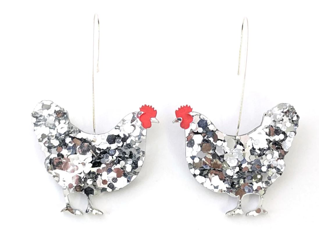 Silver chicken-shaped earrings with red combs are adorned with a glittery, speckled design. These charming Hen Glitter Dangle Earrings Silver by Blue Dog Posters feature a hooked wire for attachment, making them perfect handmade jewellery pieces.