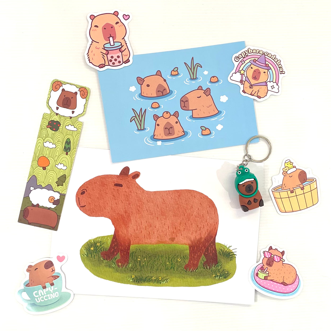 Blue Dog Posters’ Mystery Goodie Bag - Capybara includes adorable stationery and stickers with capybara illustrations, plus a keychain, bookmark, and postcard featuring swimming capybaras.
