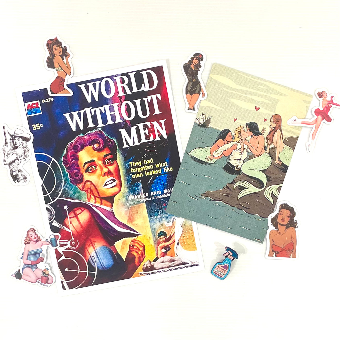 The Mystery Goodie Bag - Pin Up Girls by Blue Dog Posters features a "World Without Men" comic, a mermaids and sailors postcard, vintage pin-up girl stickers, and a perfume bottle sticker on a white background.