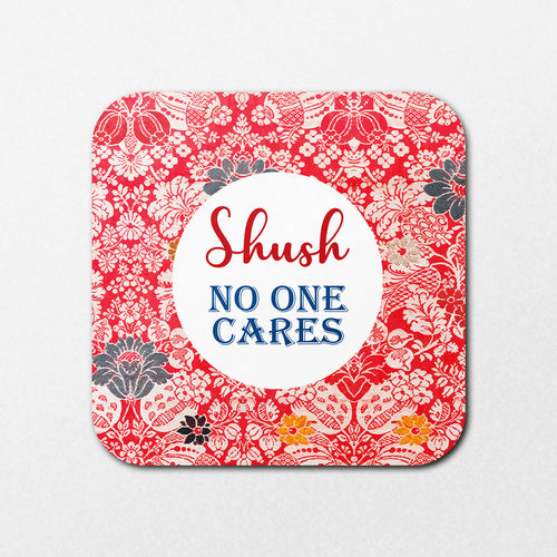The Shush Coaster by Blue Dog Posters features a red floral pattern on a square design with a white center circle that reads "Shush NO ONE CARES" in red and blue.