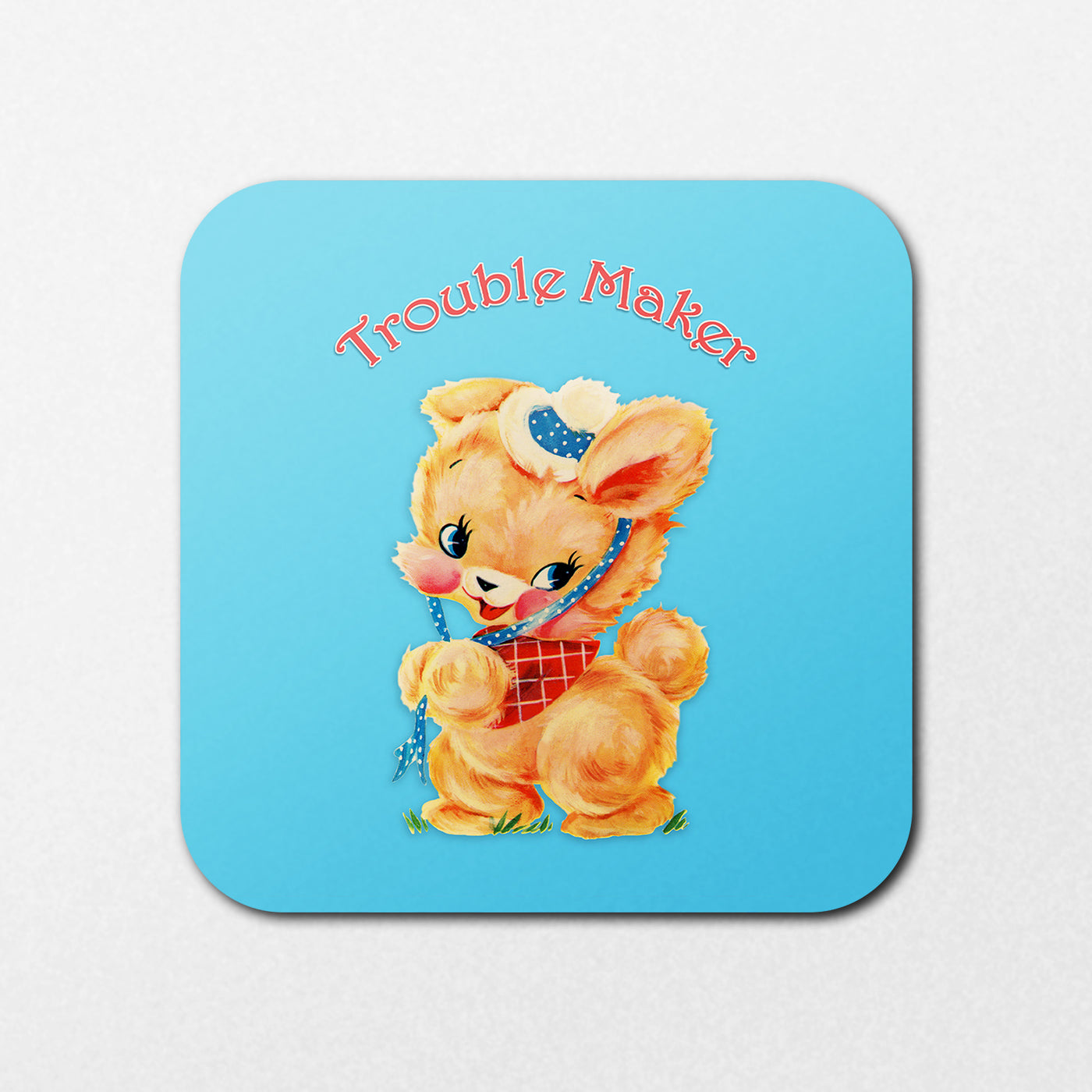 A cute cartoon bunny with a polka-dotted beret and bow tie stands on grass against a blue backdrop. "Trouble Maker" arcs overhead in red text on the Trouble Maker Coaster by Blue Dog Posters.