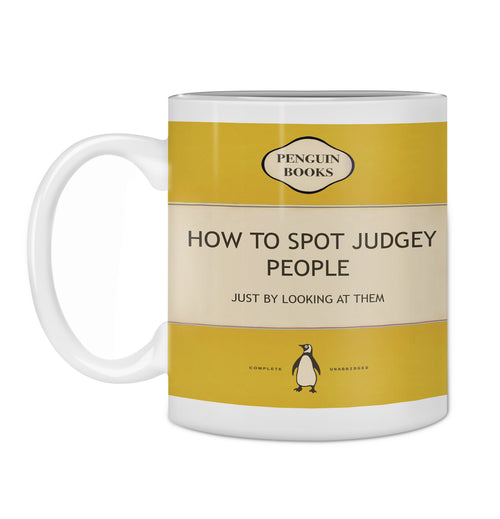 The "Hustle & Co Book Mug - Judgey People" from Blue Dog Posters' Homewares Collection features a white mug adorned with a parody book cover design in the classic yellow-striped style of Penguin Books. The title reads, "How to Spot Judgey People: Just by Looking at Them," complete with the Penguin Books logo and a penguin illustration below. Dishwasher safe.
