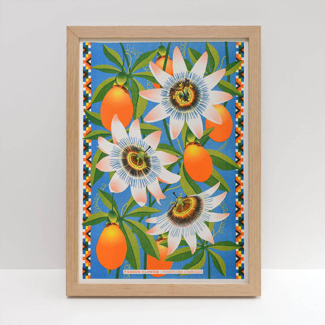 Introducing the "Passion Flower Riso" by Printer Johnson, brought to you by Blue Dog Posters. This framed artwork showcases a vibrant composition of passion flowers and orange fruits set against a bright blue background. The risograph print is enhanced with detailed green leaves and decorative borders, producing a colorful and lively piece using eco-friendly inks.