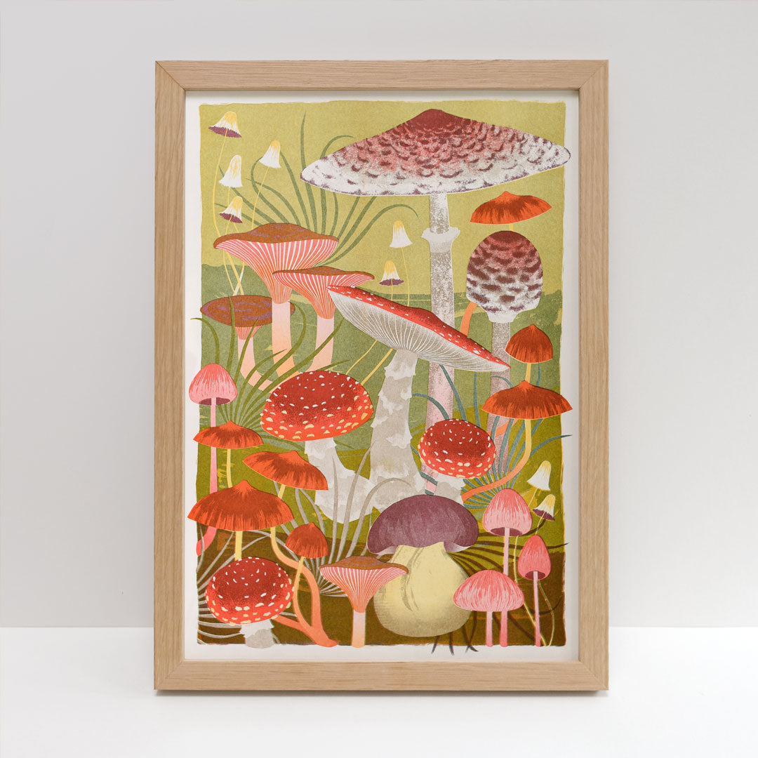 Introducing the "Fungi Riso Print by Printer Johnson" from Blue Dog Posters—a framed artwork that highlights an array of colorful mushrooms printed with eco-friendly inks. This risograph print features vibrant red, orange, and brown caps set against a lush green background, with diverse sizes and shapes adding to its whimsical appeal.