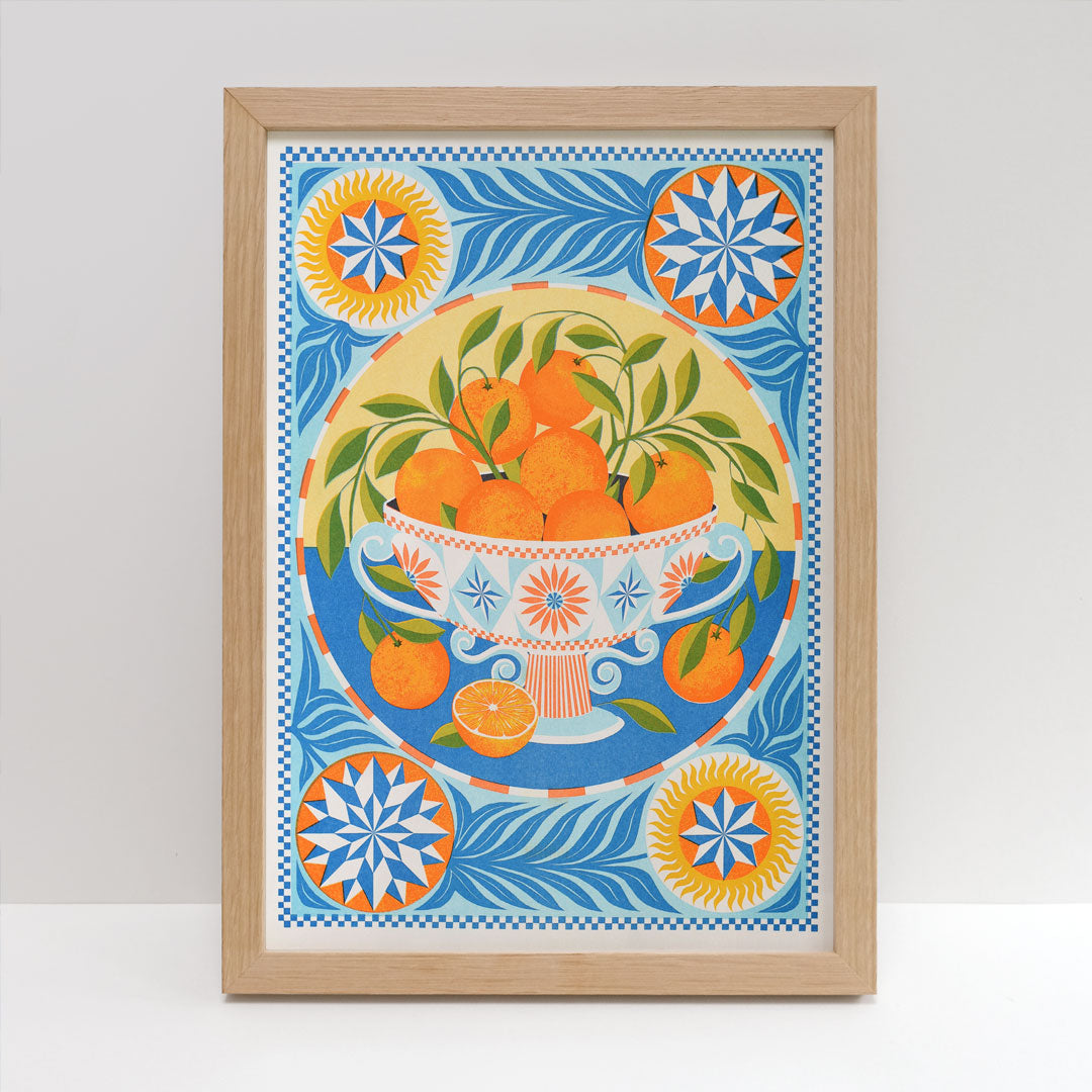 The Orange Bowl Riso Print by Printer Johnson, offered by Blue Dog Posters, is a framed Risograph artwork featuring a decorative bowl filled with oranges. It is surrounded by intricate geometric patterns in shades of blue, orange, and yellow. Crafted using eco-friendly soy-based inks, the print includes stylized leaves and star motifs in each corner.