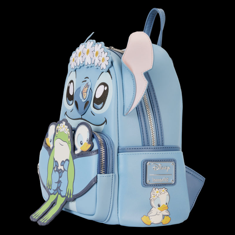 The Lilo & Stitch Springtime Mini Backpack by Blue Dog Posters features a light blue design with the face of a cartoon character, showcasing large eyes, ears, and a flower crown. The front pocket is adorned with images of a frog and a duck, each wearing flower crowns. This mini backpack is crafted from vegan leather and includes metallic Disney and Loungefly logos.