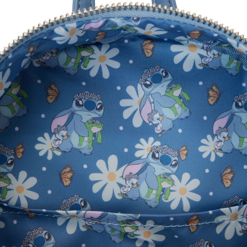 The image shows the inside of a Blue Dog Posters Lilo & Stitch Springtime Mini Backpack, lined with fabric printed with patterns of a character holding a small animal, wearing sunglasses, a flower crown, and a cape. Surrounding them are large white daisies and orange butterflies.