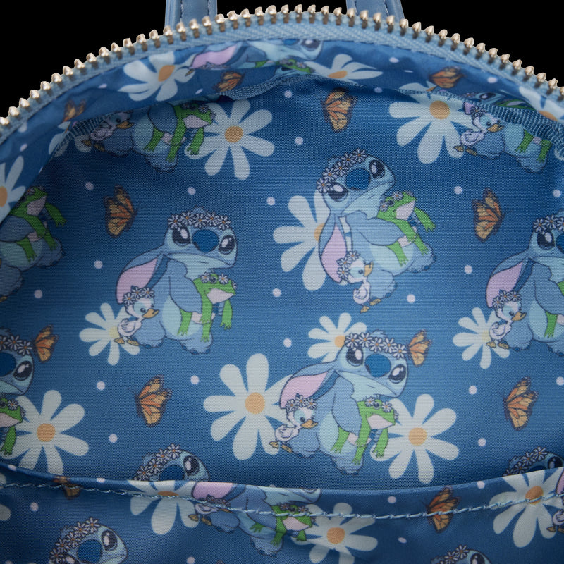 The image shows the inside of a Blue Dog Posters Lilo & Stitch Springtime Mini Backpack, lined with fabric printed with patterns of a character holding a small animal, wearing sunglasses, a flower crown, and a cape. Surrounding them are large white daisies and orange butterflies.