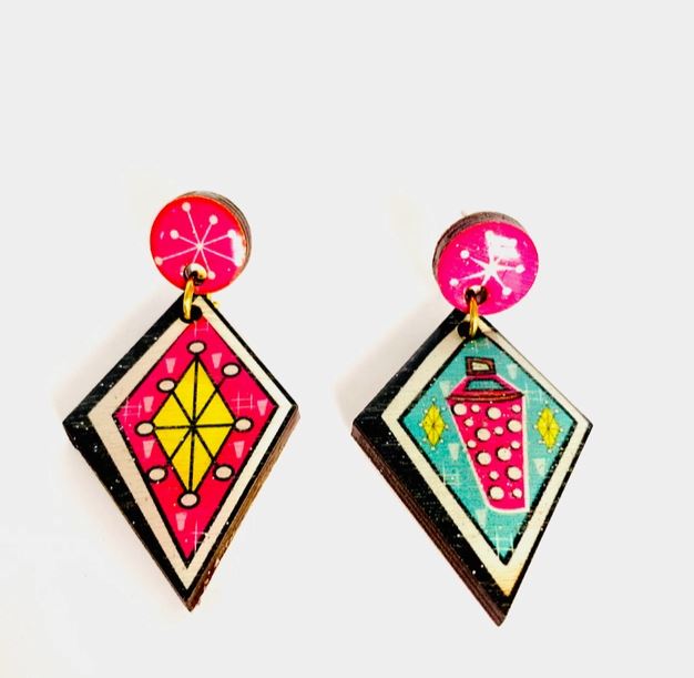 The Atomic Retro Earrings by Blue Dog Posters include a pair of geometric earrings: one with a yellow diamond pattern on a pink background and the other with a pink shaker design on a teal background, both affixed to pink circular studs.