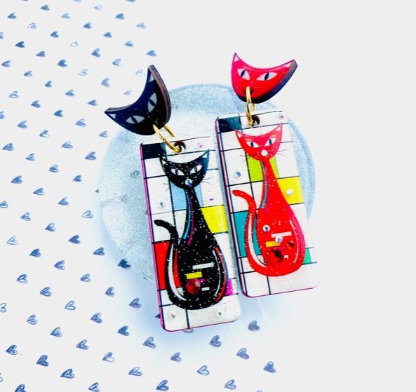 The Atomic Cat Retro Earrings by Blue Dog Posters feature colorful abstract cat designs, one in black and the other in red, on rectangular pendants with geometric patterns against a heart-patterned background.