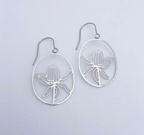The Denz Mini Banksia Earrings Silver by Blue Dog Posters are a pair of silver oval earrings that belong to the Native Flora collection. These earrings feature intricate flower designs on a plain white background and are crafted from recycled stainless steel, resembling blossoming flowers for an elegant and minimalist style.