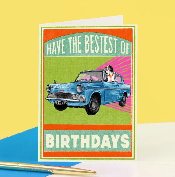 The Bestest Birthday Car Greeting Card by Blue Dog Posters showcases a vibrant design with a dog in sunglasses and a scarf, driving a blue vintage car. The text "HAVE THE BESTEST OF BIRTHDAYS" stands out on the bright background, accompanied by a nearby pen.