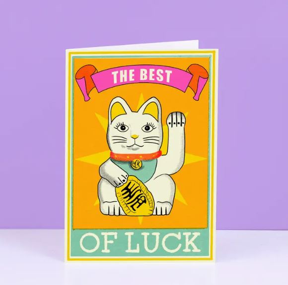 Blue Dog Posters presents "The Best of Luck" Cat Greeting Card: A colorful card featuring a waving Maneki-neko on an orange background. It reads "The Best" with a pink ribbon and "Of Luck" in bold white letters on turquoise.