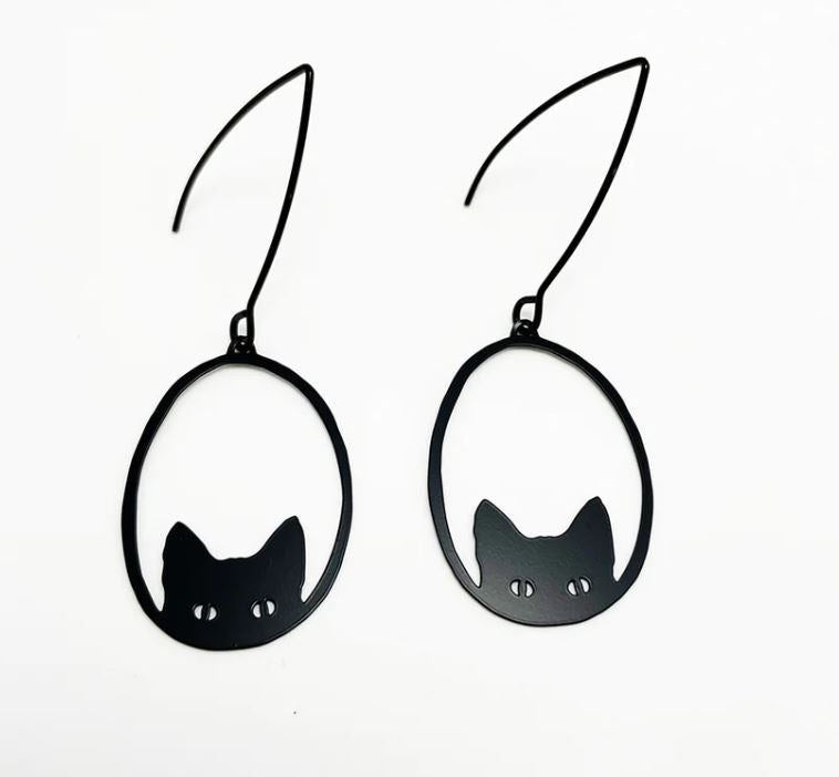 Introducing the Denz Mini Earrings Black Cat by Blue Dog Posters: Each pair of these lightweight earrings is crafted from recycled plated stainless steel, showcasing a minimalist and whimsical design. These earrings feature a simple, black silhouette of a cat head with pointed ears and circular cut-out eyes, all enclosed within a thin, black oval frame.