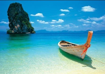 A small wooden boat is gently anchored in the clear, shallow waters of a tropical beach. The turquoise sea extends to the horizon, where a large, lush, rocky island rises abruptly from the water under a bright blue sky with scattered white clouds—truly a scene worthy of Blue Dog Posters' Phuket Beach Boat GIANT Poster.