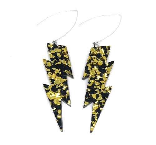 The Lightning Bolt Gold Black Earrings by Blue Dog Posters feature an eye-catching pattern of gold and black flecks. These handmade jewellery pieces are attached to thin silver wires, giving them a sleek and modern appearance. This bold and striking design is perfect for making a statement.
