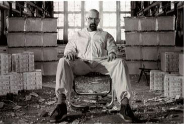 A person with a shaved head and beard sits on a chair in a dimly lit, packed warehouse, surrounded by stacks of money and large containers. The environment looks stressful, with discarded bills and a disheveled floor suggesting intense activity or chaos—a scene straight out of the "Breaking Bad All Hail the King" TV show by MTV 354.