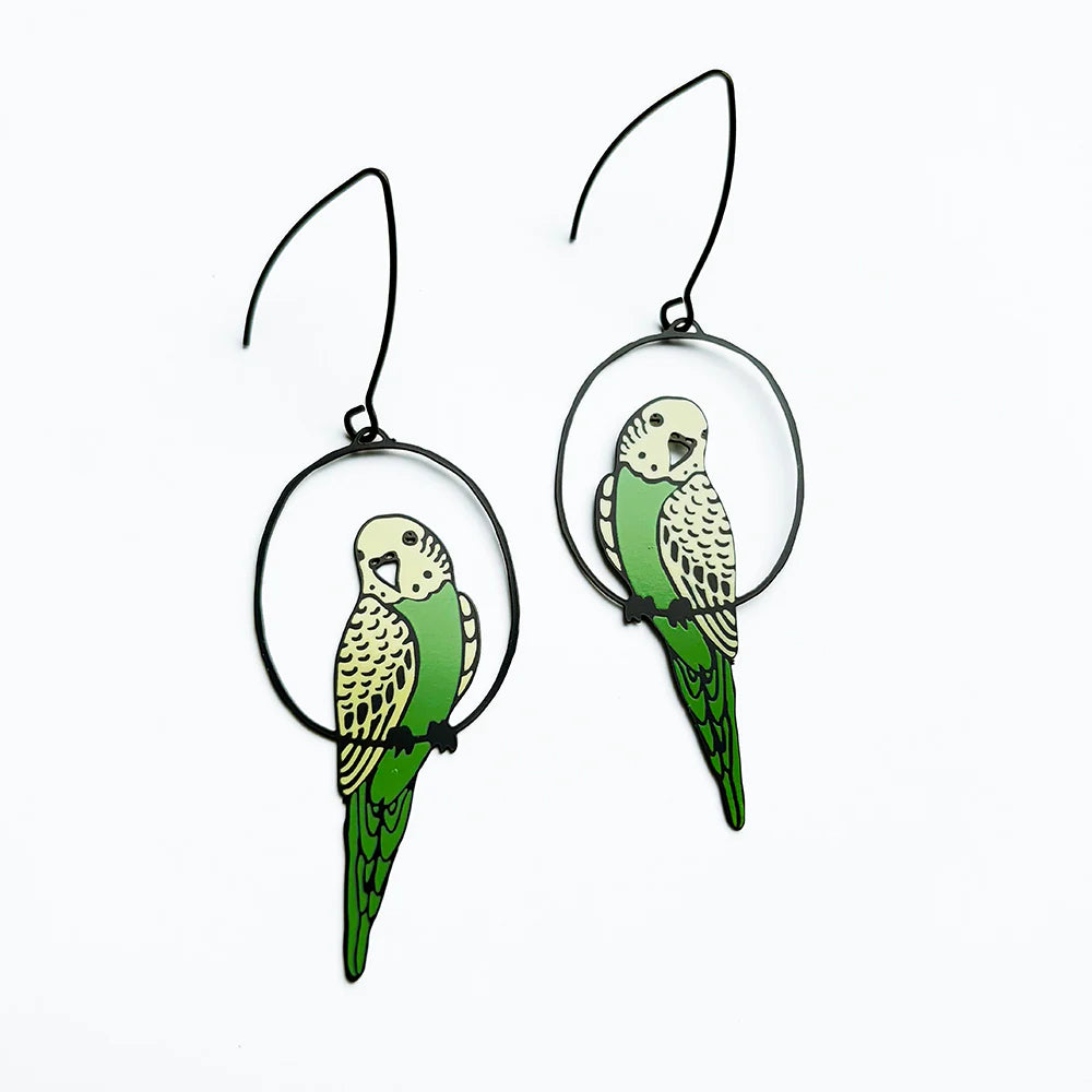 The Budgie Black Green Yellow Denz Earrings by Blue Dog Posters feature green and yellow parakeet designs perched in black hoops, shown on a white background.