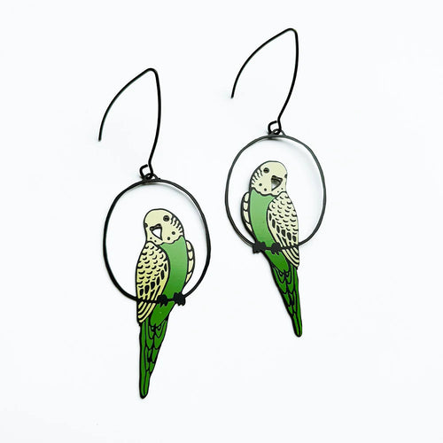 The Budgie Black Green Yellow Denz Earrings by Blue Dog Posters feature green and yellow parakeet designs perched in black hoops, shown on a white background.