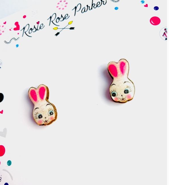 The Cute Retro Bunny Stud Earrings by Blue Dog Posters showcase two small bunny-shaped earrings with pink ears and cheerful faces on a card adorned with colorful dots, hearts, and the name "Rosie Rose Parker" at the top.