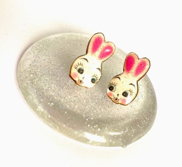 The Cute Retro Bunny Stud Earrings by Blue Dog Posters feature small, vintage-style cartoon bunny faces with pink ears and rosy cheeks on a glittery, translucent domed surface.