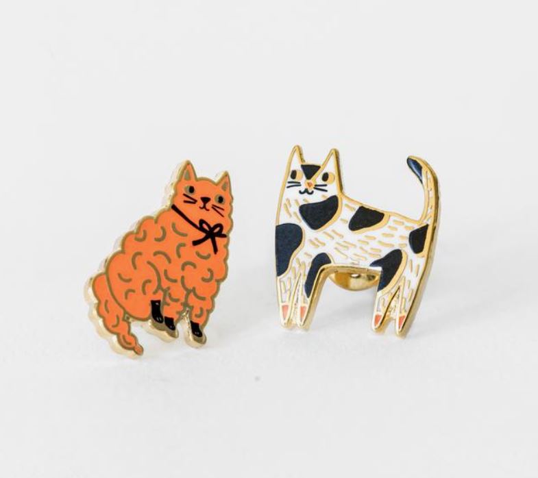 Product Description: The Cats Earrings by Blue Dog Posters showcase two charming enamel pins depicting cats. One is a fluffy orange cat adorned with a black bow tie, while the other is a graceful white cat with black and tan patches. Both designs feature elegant gold outlines and hypoallergenic posts, making them ideal for sensitive ears. These beautiful earrings are set against a plain white background.