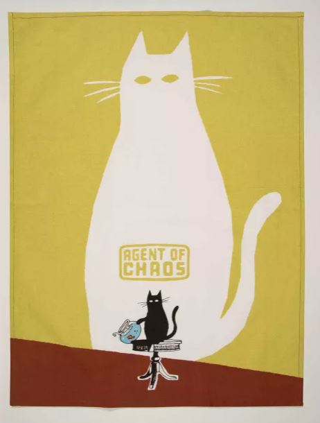 The Agent of Chaos Dish Towel by Blue Dog Posters showcases a graphic design featuring a large white cat with glowing eyes, labeled "Agent of Chaos" in yellow text. In front of the white cat, there's a smaller black cat standing on a stack of books while holding a TV set. The background is yellow and transitions to brown at the bottom, reflecting the same high quality as our cotton tea towels from the Homewares Collection.