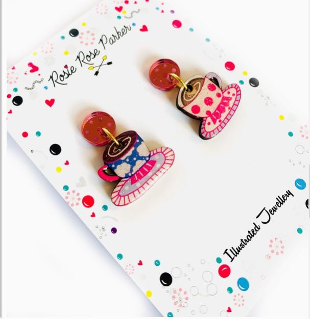 Colorful teacup earrings with saucers and a floral pattern, displayed on a decorative card labeled "Rose Rose Parker Illustrated Jewelry," are actually called Coffee Cup Retro Earrings by Blue Dog Posters.