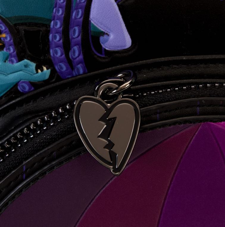 Close-up of a black and purple zipper on the Disney Villains Curse Your Hearts Mini Backpack by Blue Dog Posters, with a heart-shaped charm hanging from it. The charm, reminiscent of Disney Villains, is black with a silver outline and split by a lightning bolt. Purple and teal fabric surround the zipper, embodying the "Curse Your Hearts" vibe.