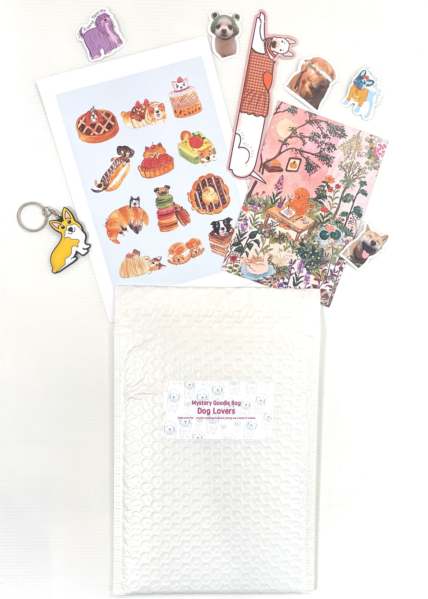 A flat lay of the Mystery Goodie Bag - Dog Lover by Blue Dog Posters features illustrated dog stickers, postcards, a dog keychain, and a bookmark beside a white bubble mailer labeled for dog lovers.