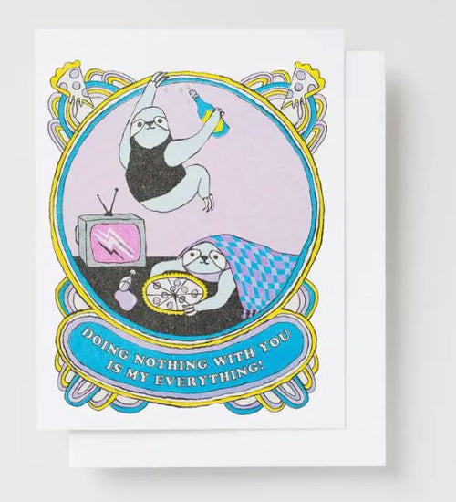 The Doing Nothing With You Risograph Card from Blue Dog Posters showcases two charming illustrated sloths. One sloth is lounging on a couch, snacking and watching TV, while the other descends with a drink in hand. A banner beneath them declares, "Doing nothing with you is my everything." The whimsical border adds to the card's charm, and it is printed on recycled paper.