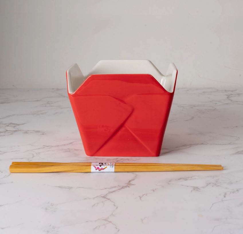 The Blue Dog Posters Takeout Box Serving Bowl With Chopsticks GOLD DRAGON, a red ceramic bowl, sits on white marble with wooden chopsticks in front. Stylish and microwave safe, it’s perfect for convenient dining at home.