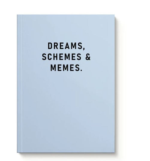An A5 soft cover notebook from Blue Dog Posters, titled "Dreams, Schemes & Memes," with a light blue cover featuring bold black lettering, stands upright against a white background.
