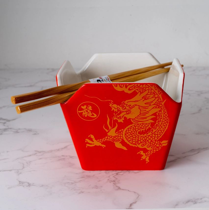 The Blue Dog Posters Takeout Box Serving Bowl With Chopsticks GOLD DRAGON, a red hexagonal microwave-safe container with a gold dragon design, sits open on marble with wooden chopsticks resting across the top.