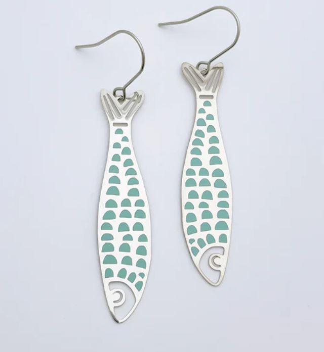 A pair of Blue Dog Posters' Denz Midi Fishy Silver Blue Earrings, featuring elegant aqua blue scale patterns. Lightweight and crafted from recycled stainless steel, these silver earrings showcase a fish design with a cutout tail and head, along with a curved wire hook for easy wearing. The background is plain white.