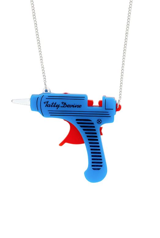 This whimsical Glue Gun Necklace, designed by Blue Dog Posters, features a vibrant pendant shaped like a blue and red toy ray gun with "Tatty Devine" inscribed on it. Made from recycled acrylic, the pendant dangles from a sparkling silver chain, bringing a splash of color to any ensemble.