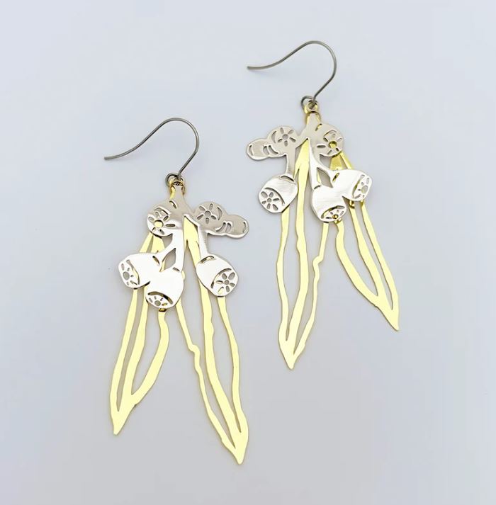 The Gumnut and Leaf Gold Silver Denz Earrings by Blue Dog Posters showcase elegant floral and leaf-like designs with delicate cut-out patterns. Their sleek hooks complement the intricate artistry of these exquisite drop earrings.