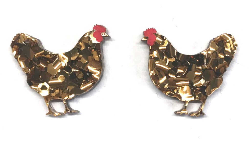 Two rooster-shaped earrings, the Hen Glitter Stud Earrings Bronze by Blue Dog Posters, are made of a gold-colored, glittery material with red combs. The roosters face each other against a white background.
